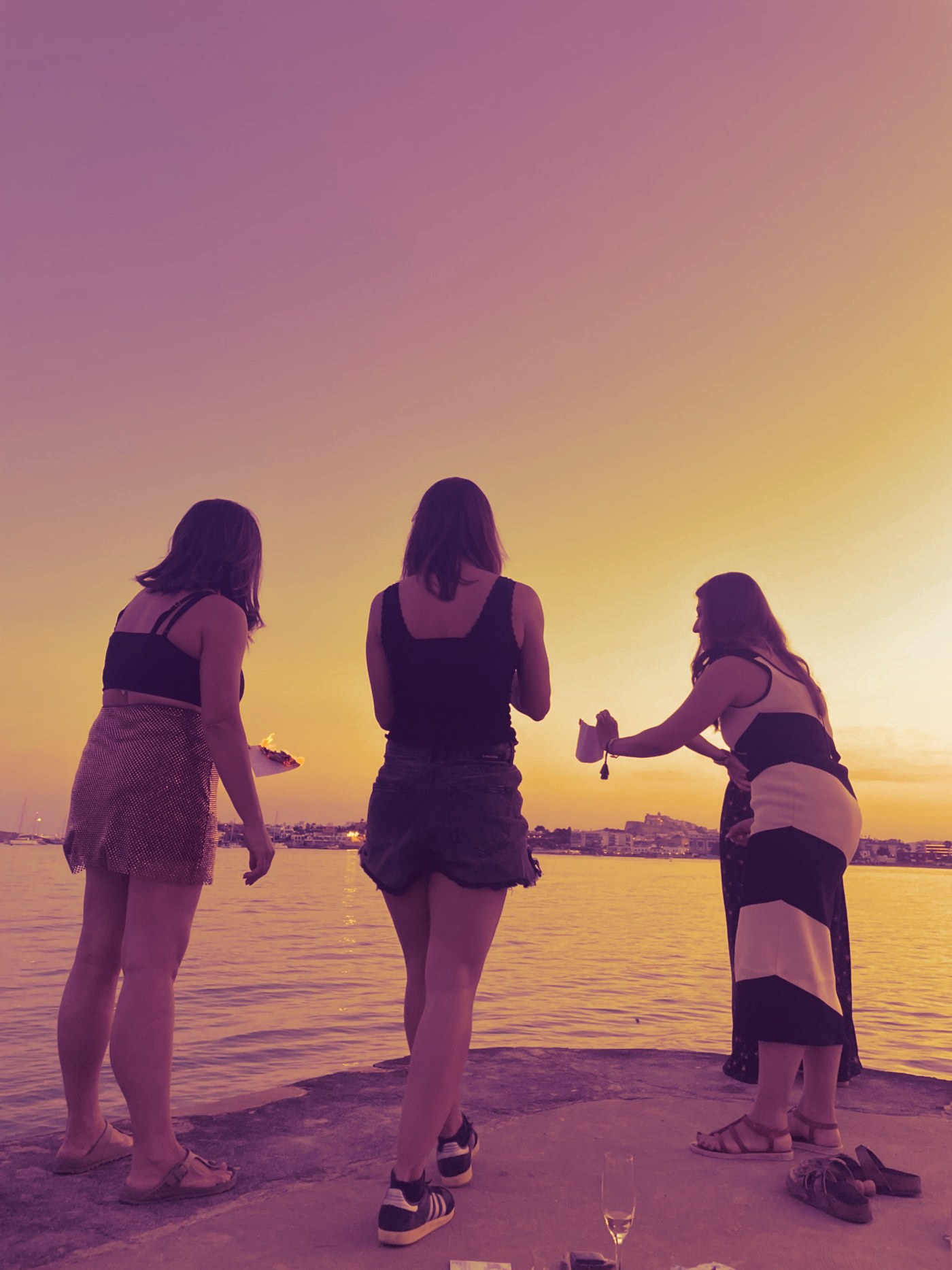Three women burning handwritten letters at sunset by the sea in Ibiza